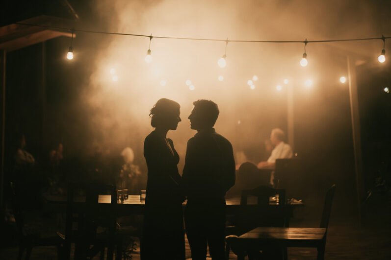 Photographie de mariage,Silhouettes de mariés dansant sous les guirlandes lumineuses lors d'une réception de mariage en soirée avec du brouillard